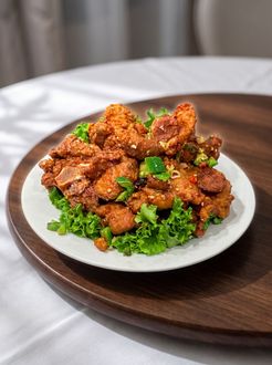 Plate of crispy fried chicken garnished with green onions on a white plate atop a wooden tray
