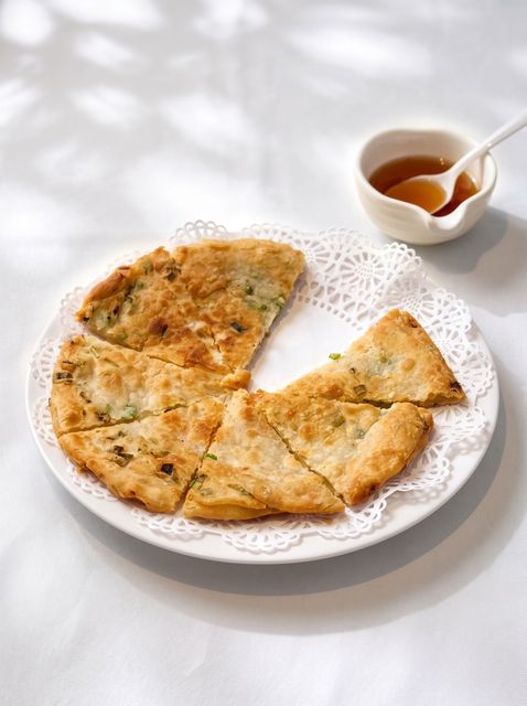 Sliced flatbread on a white lace doily, with a small bowl of dipping sauce on a white surface.