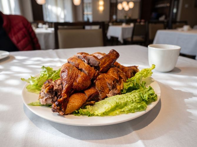Roasted chicken on lettuce on a white plate in a restaurant, with a white cup in the background