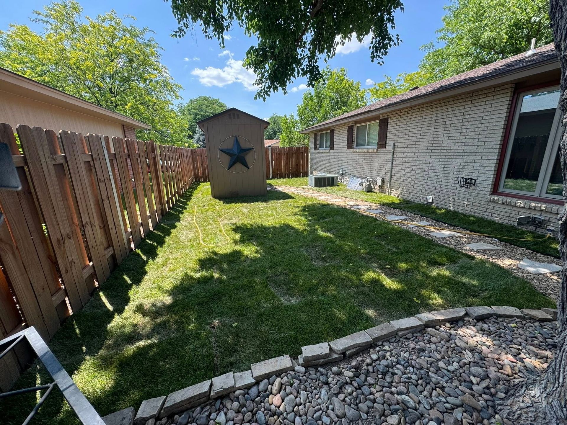 Backyard patio and lawn between a wooden fence and house, with a small shed marked by a star.