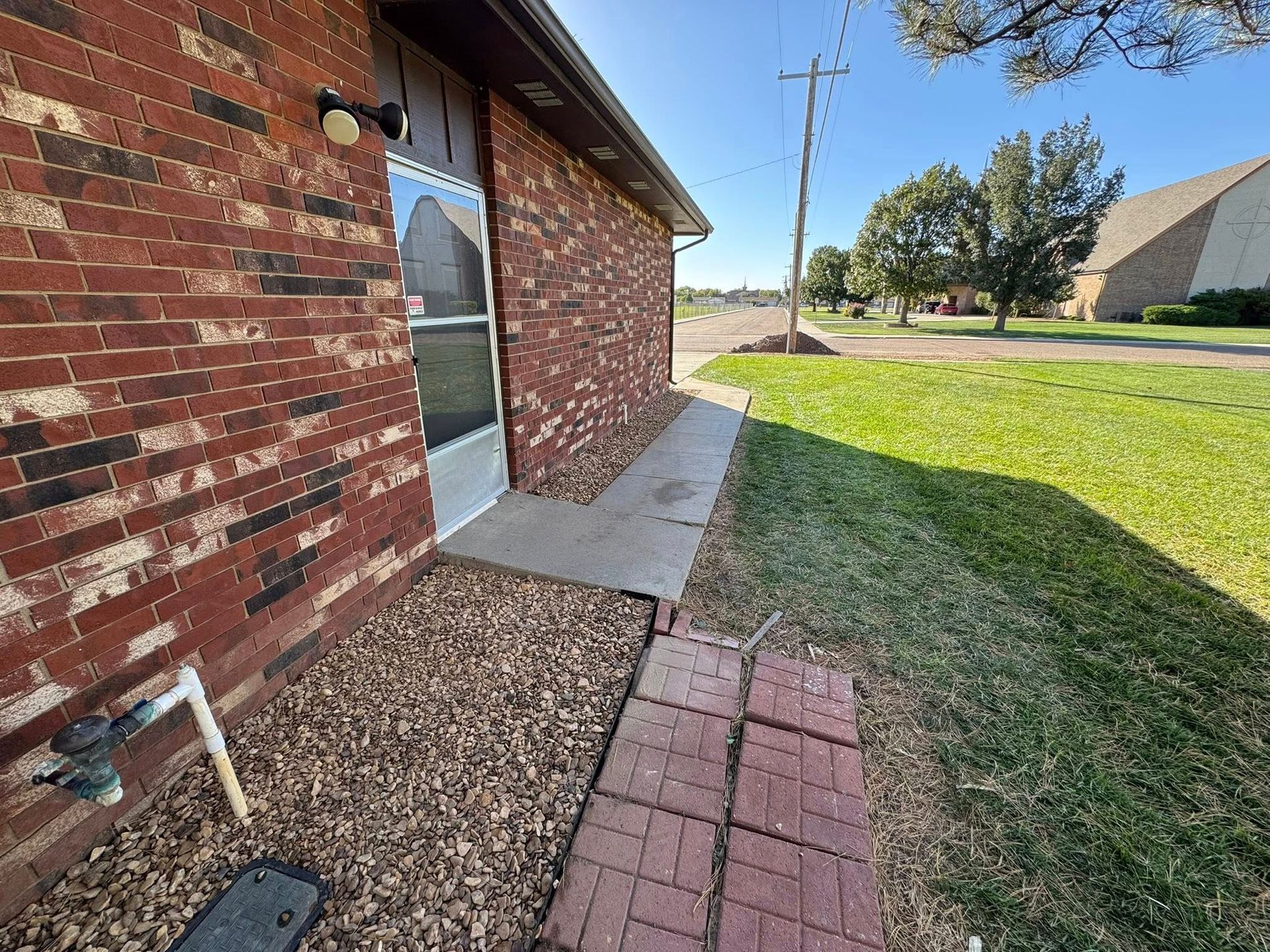 Brick house side yard with glass door, concrete walkway, gravel bed, and grassy lawn.