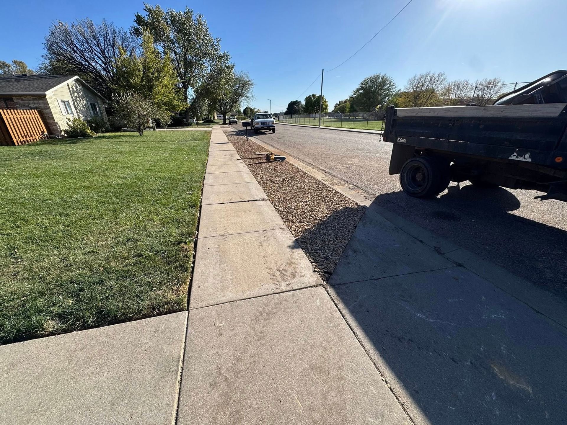 Residential sidewalk beside grassy yard and parked truck on a sunny street