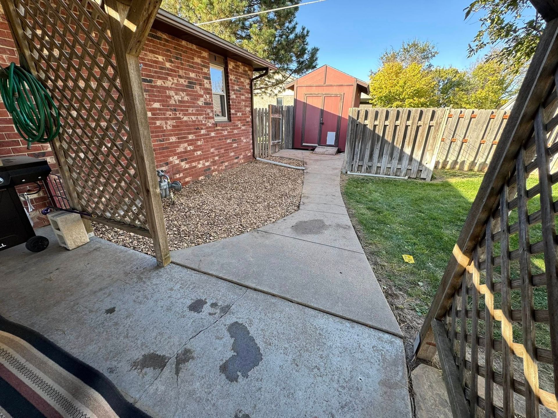 Backyard concrete walkway beside a red brick house, lattice fence, and small grass strip