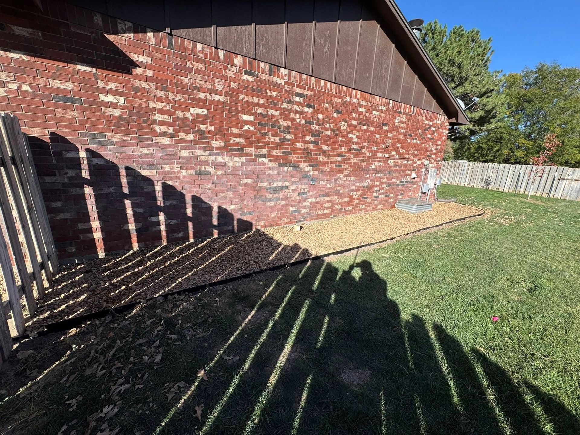 Brick house side yard with grass, wooden fence shadows, and a sloping roofline