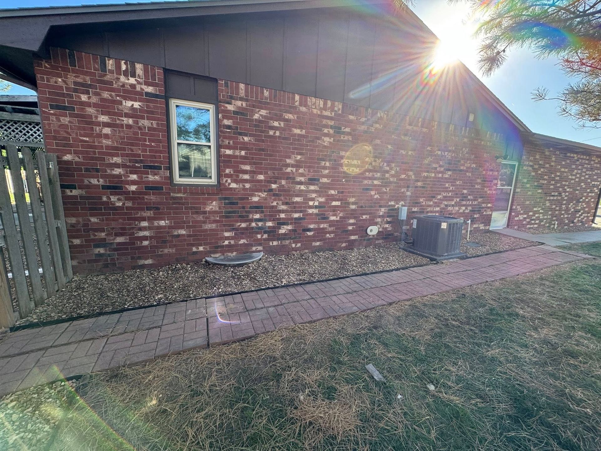 Brick house exterior with a window, front walkway, and bright sun flare on the roofline