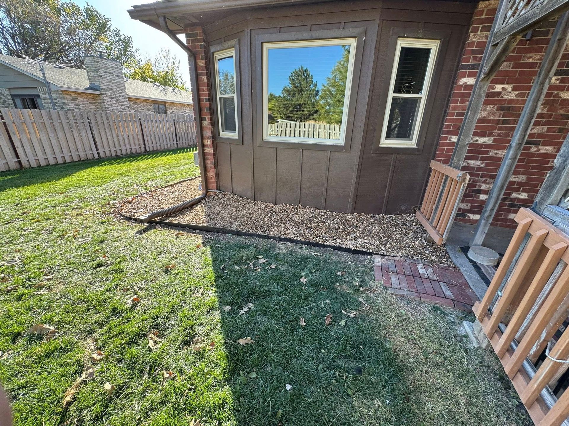Backyard patio beside a brick house, with a window, stone border, and grass lawn.