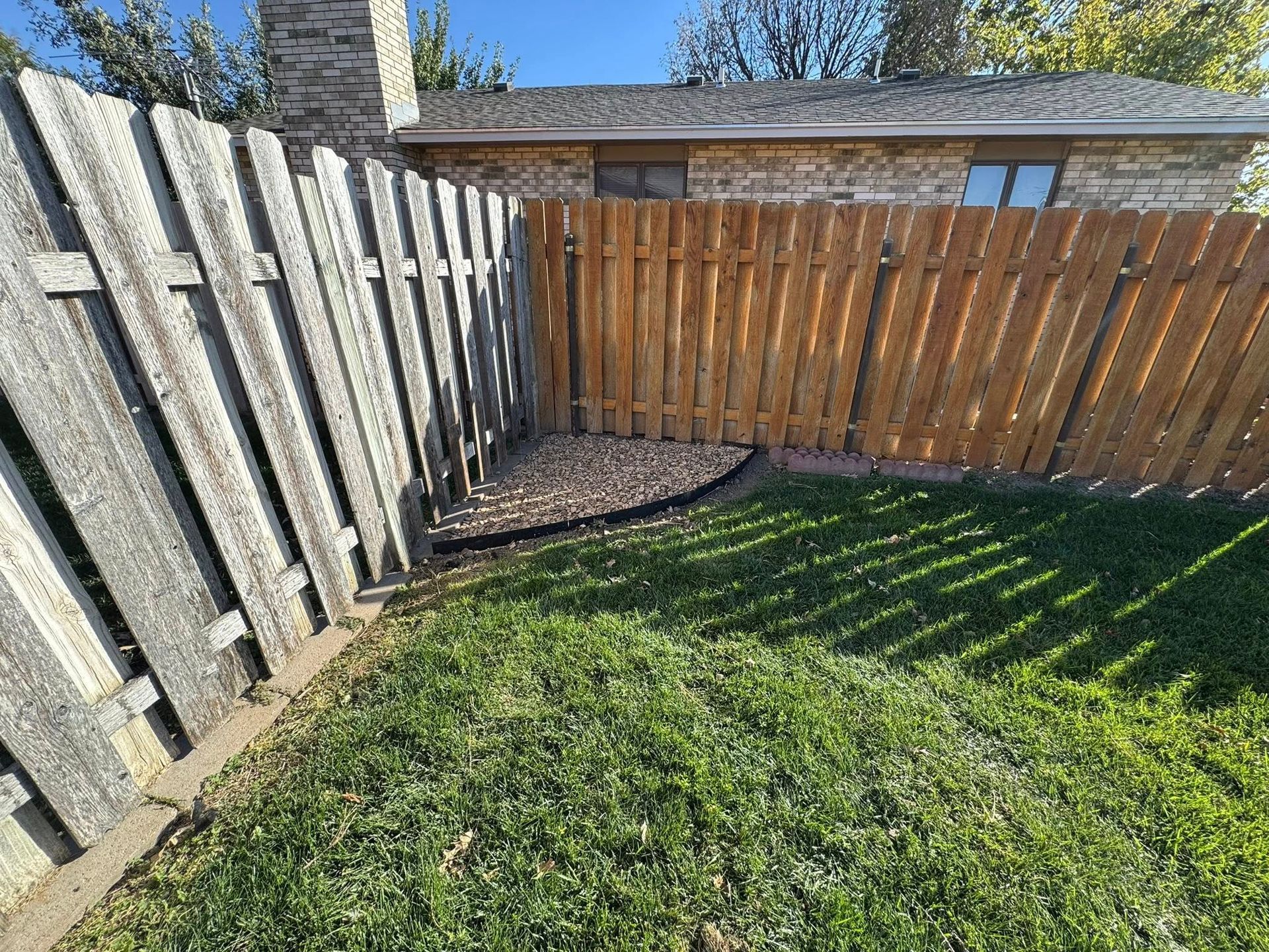 Backyard corner with wooden fences, green grass, and a small deck or shed in the background