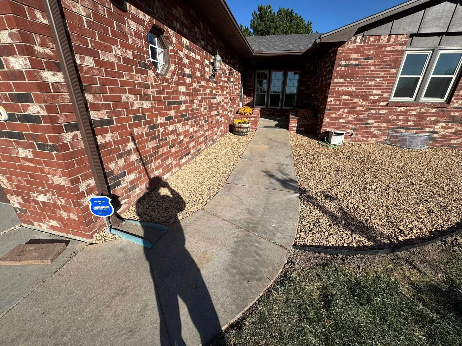 Front walkway between red brick houses, with a concrete path, gravel beds, and a small blue security sign.