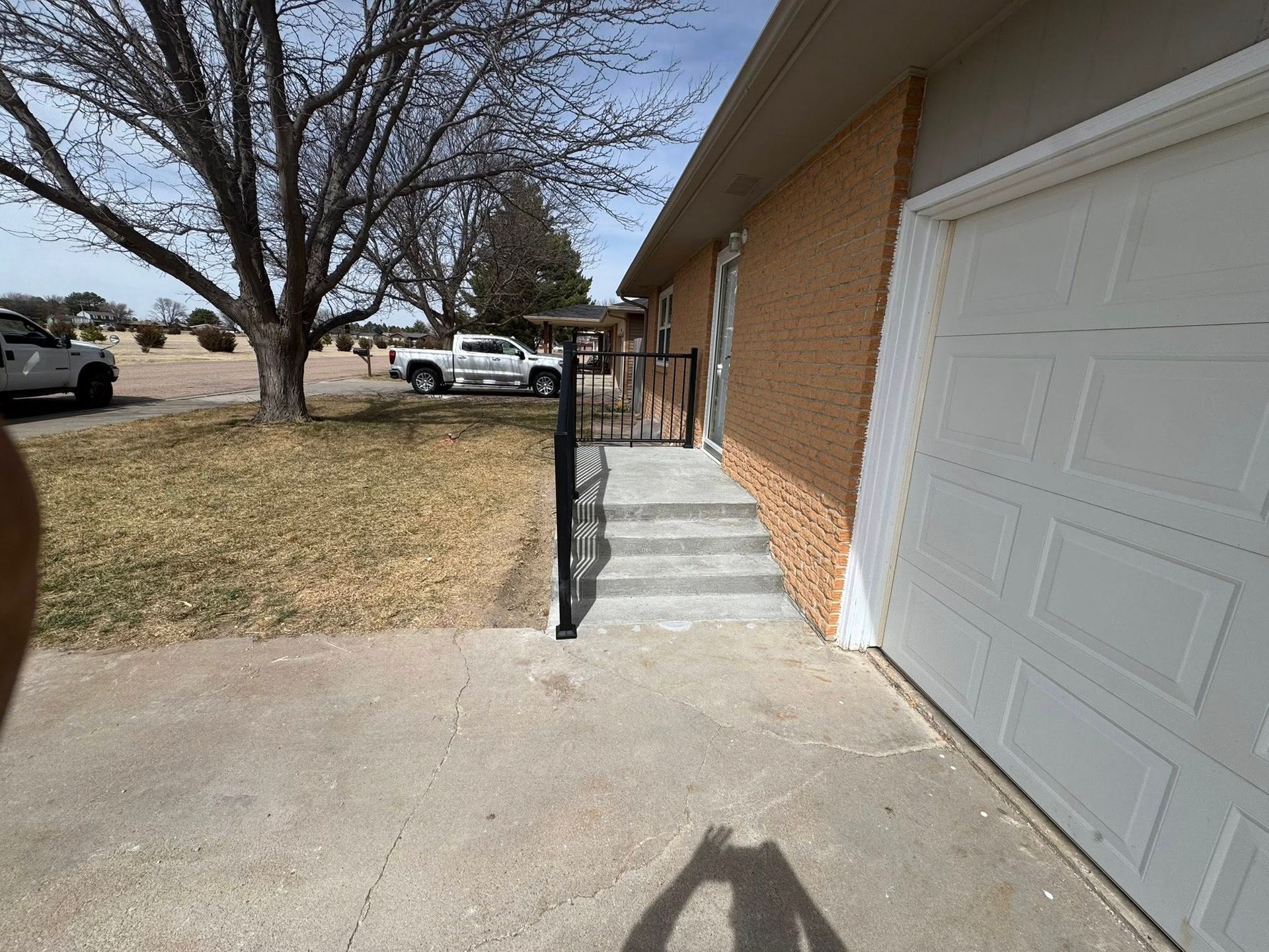 Apartment walkway with concrete steps, black handrails, brick wall, and a white garage door outside.