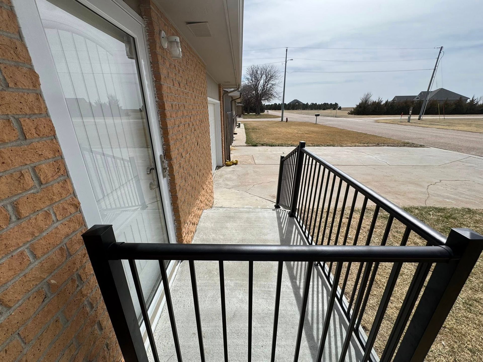 Brick building entrance with black metal railing beside a concrete walkway and road.