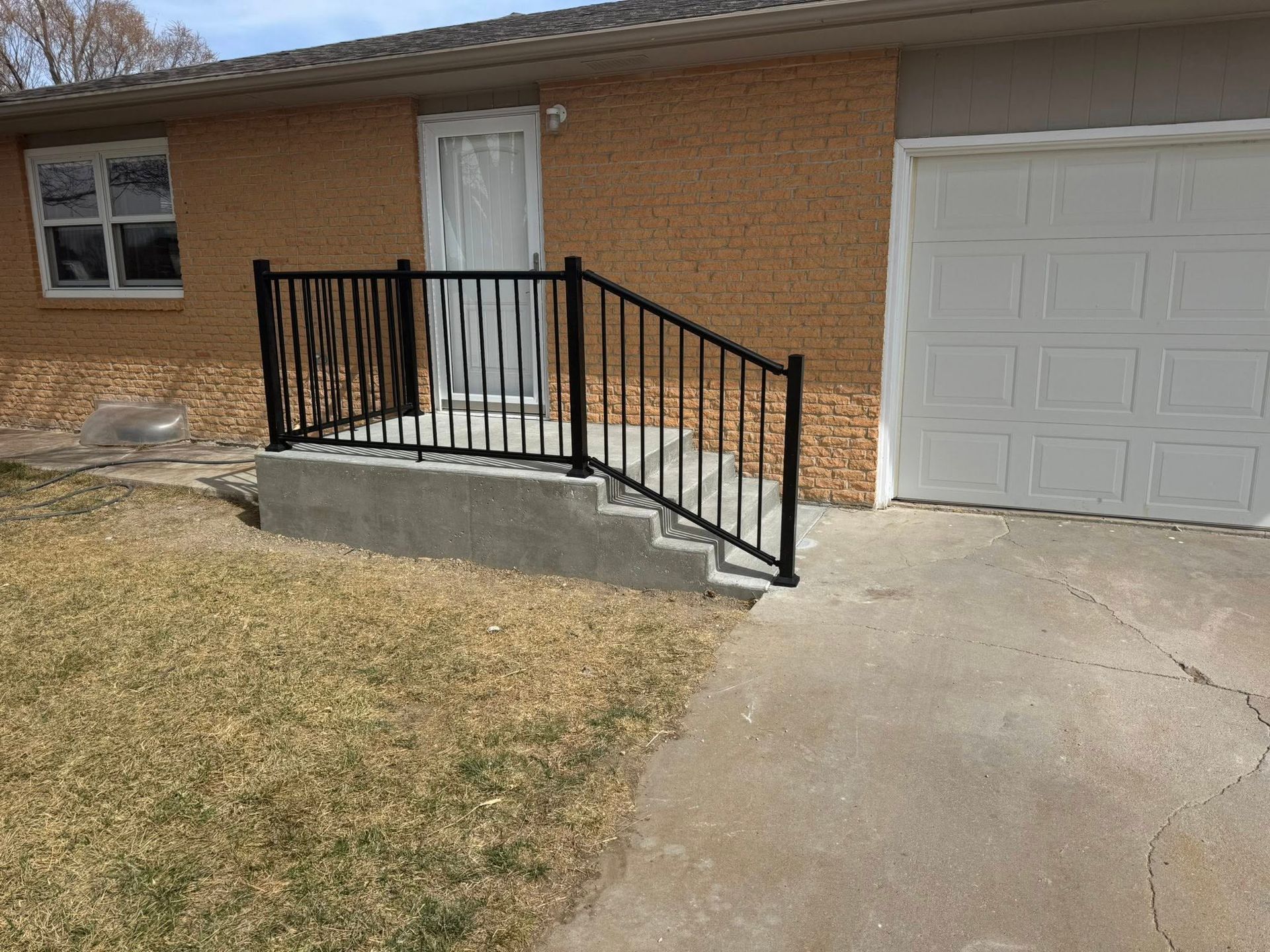 Brick house entrance with white door, black railing ramp, and driveway beside garage