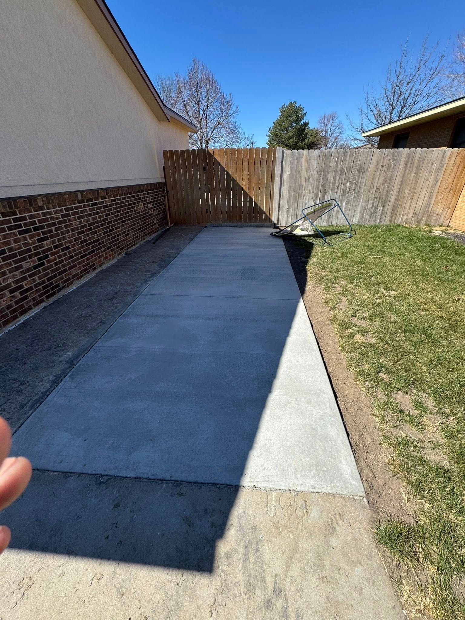 Concrete backyard patio beside house and lawn, leading to a wooden fence and gate.