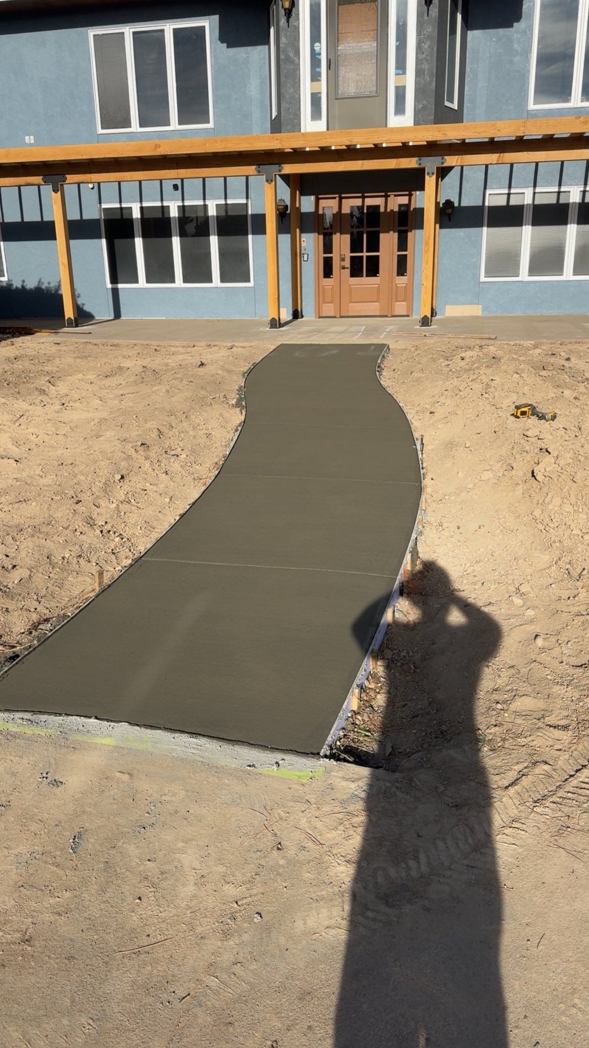 Fresh concrete walkway leading to a house entrance with unfinished dirt yard and orange trim