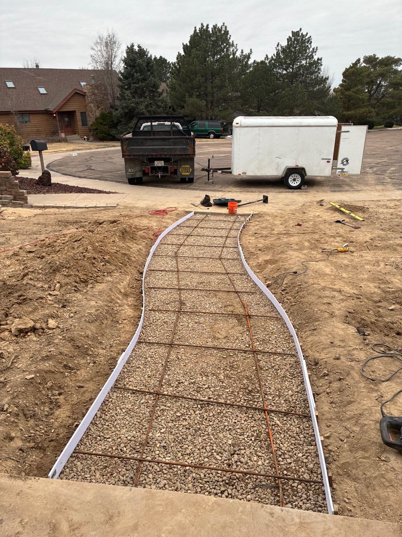 Concrete walkway form in progress at a construction site with trucks and a white trailer in the background