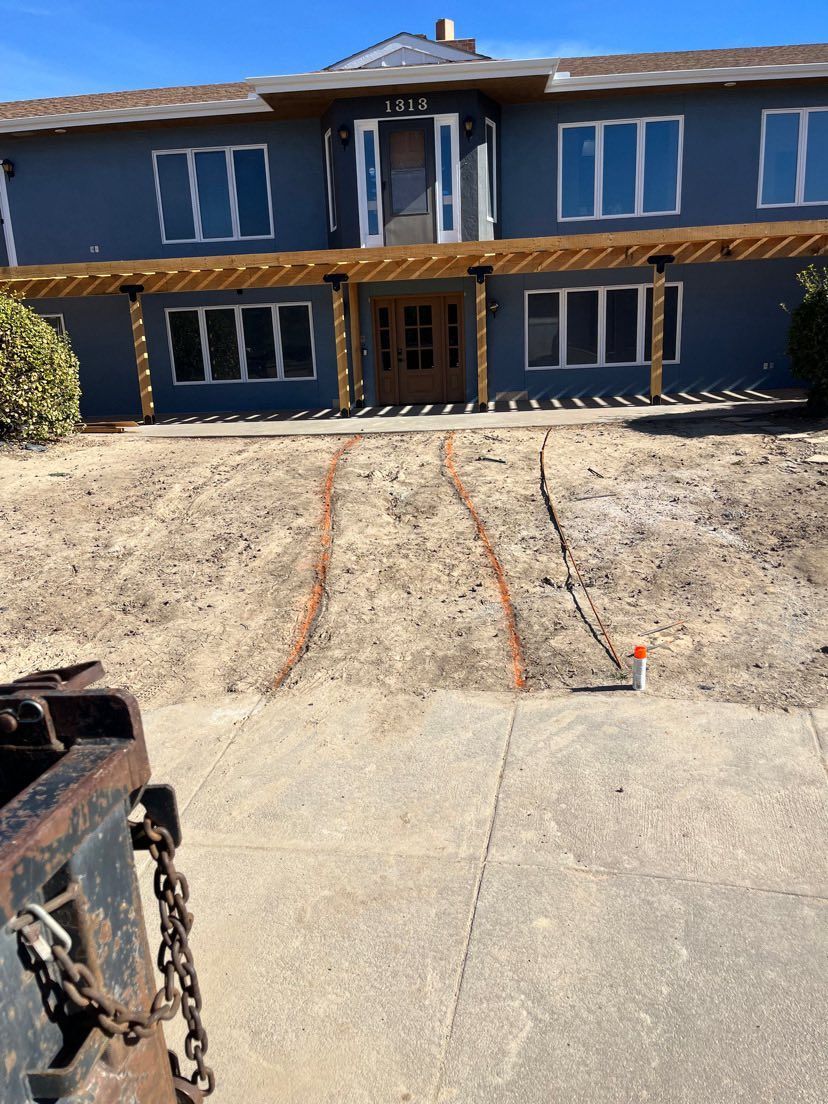 Two-story blue house with concrete driveway and dirt front yard under construction