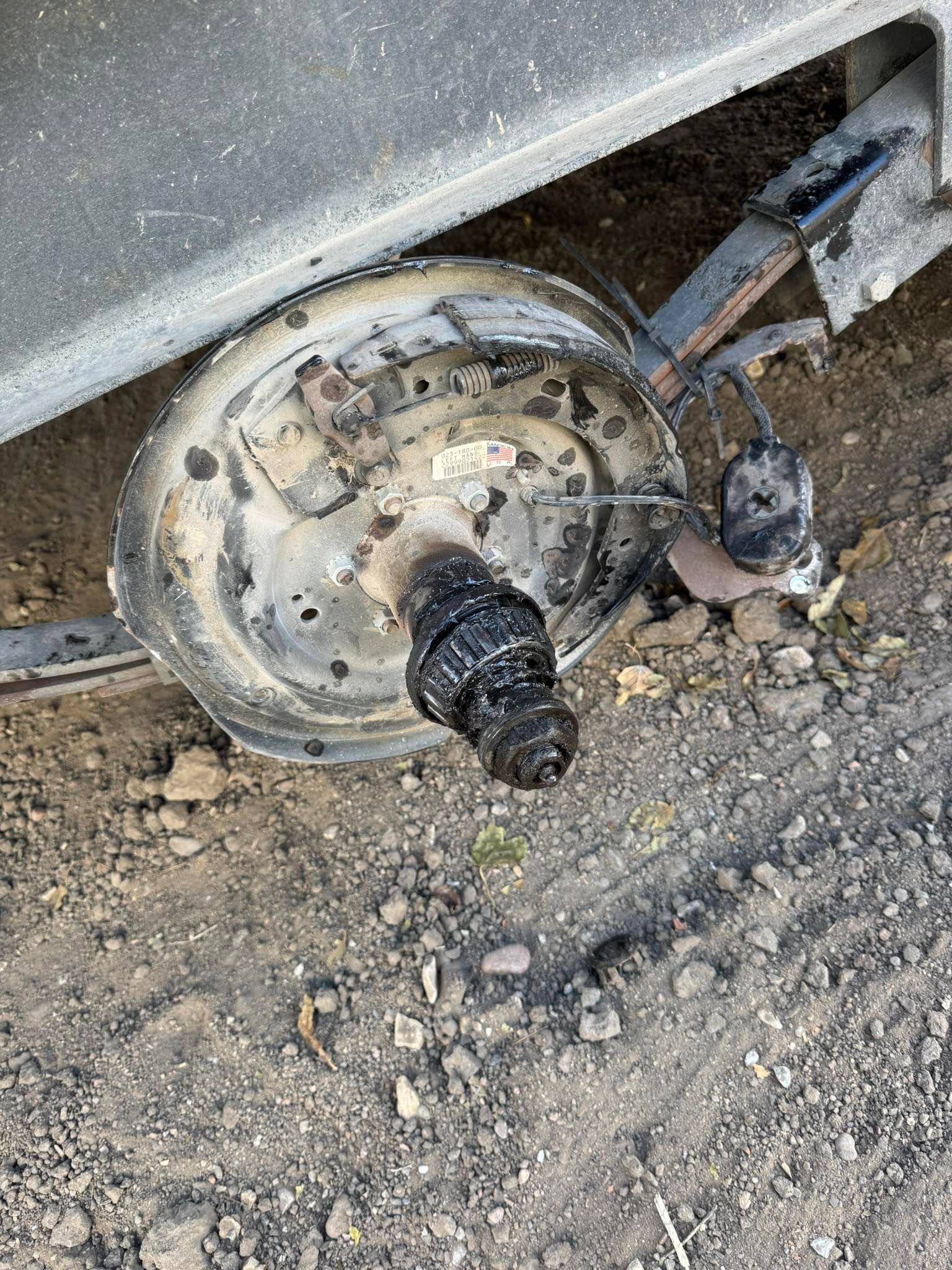 Damaged wheel hub and axle under a vehicle, with rust and dirt on the ground.