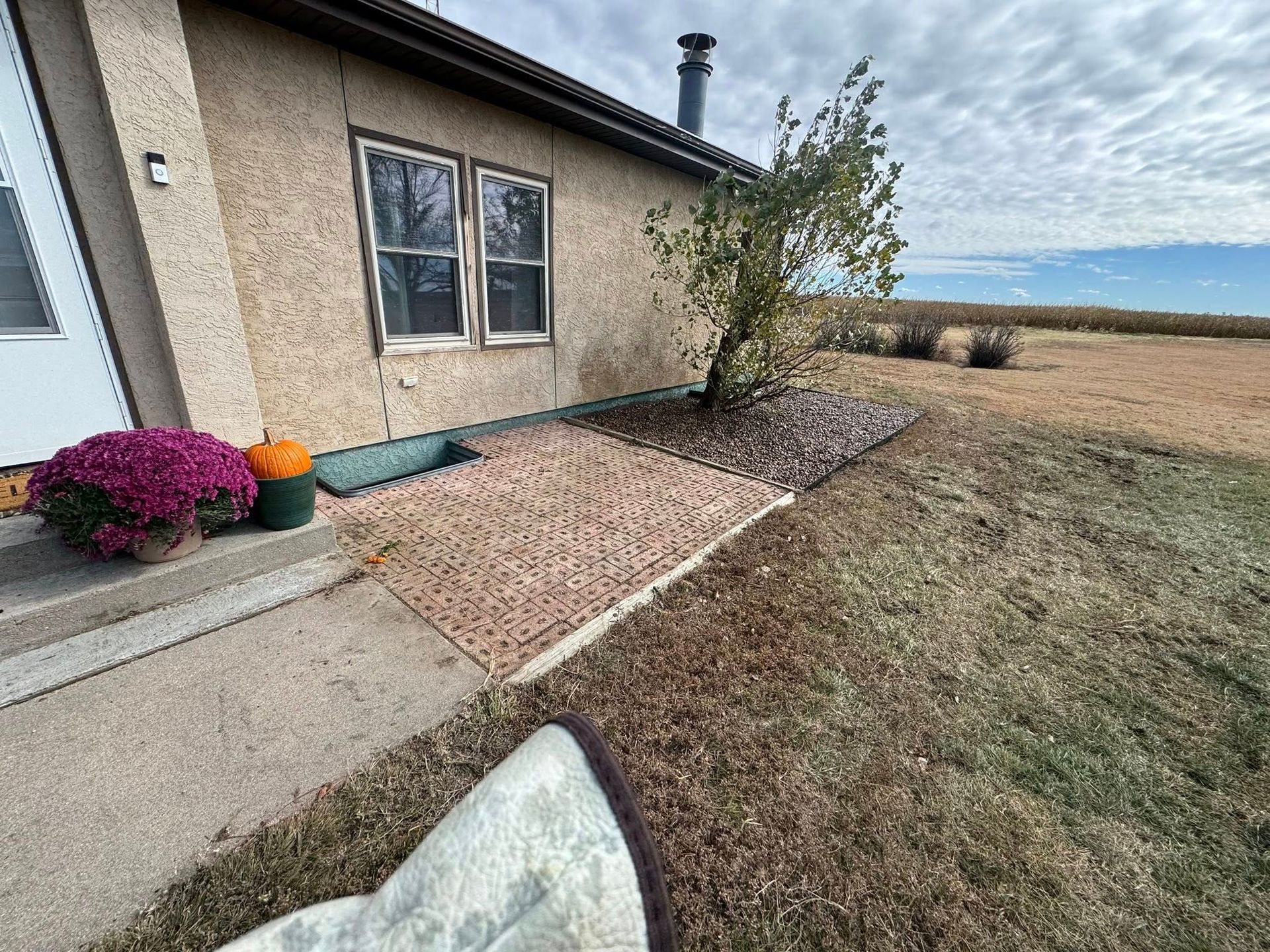 House exterior with gravel walkway, concrete path, flower bush, and grassy yard under cloudy sky