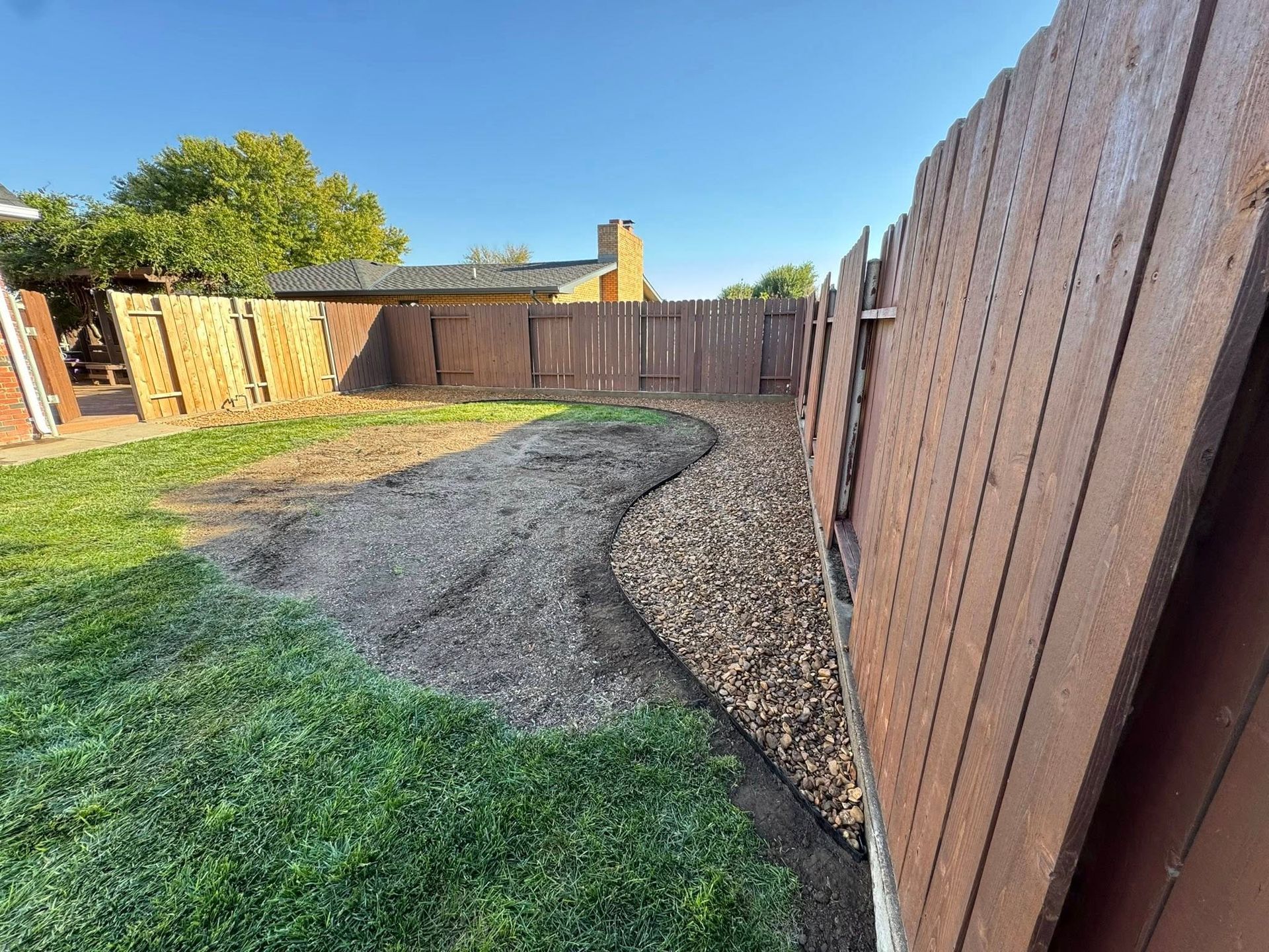 Backyard with grass, gravel path, wooden fence, and shed in warm sunlight