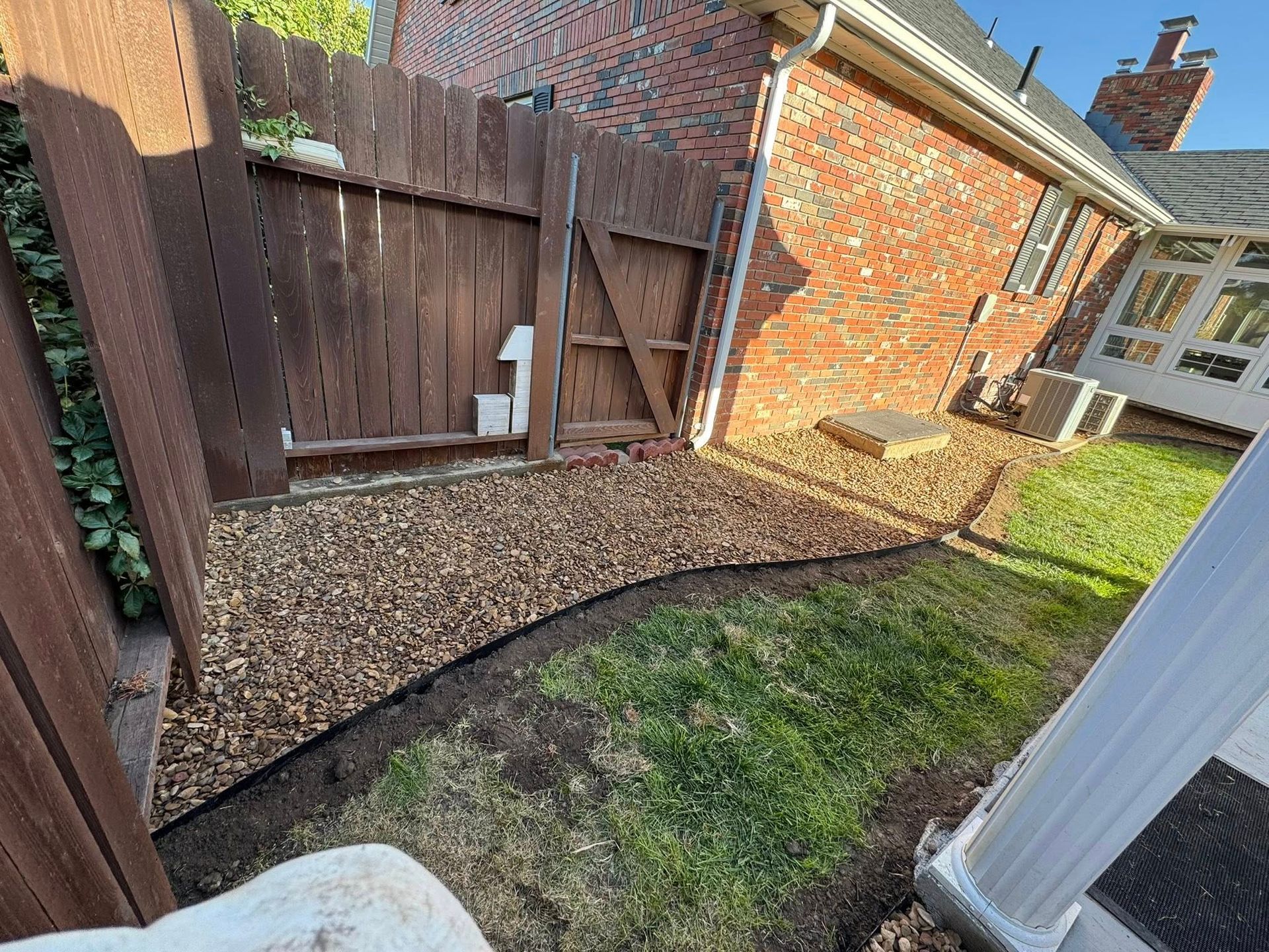 Narrow backyard with gravel path, grass patch, wooden gate, and brick house wall.