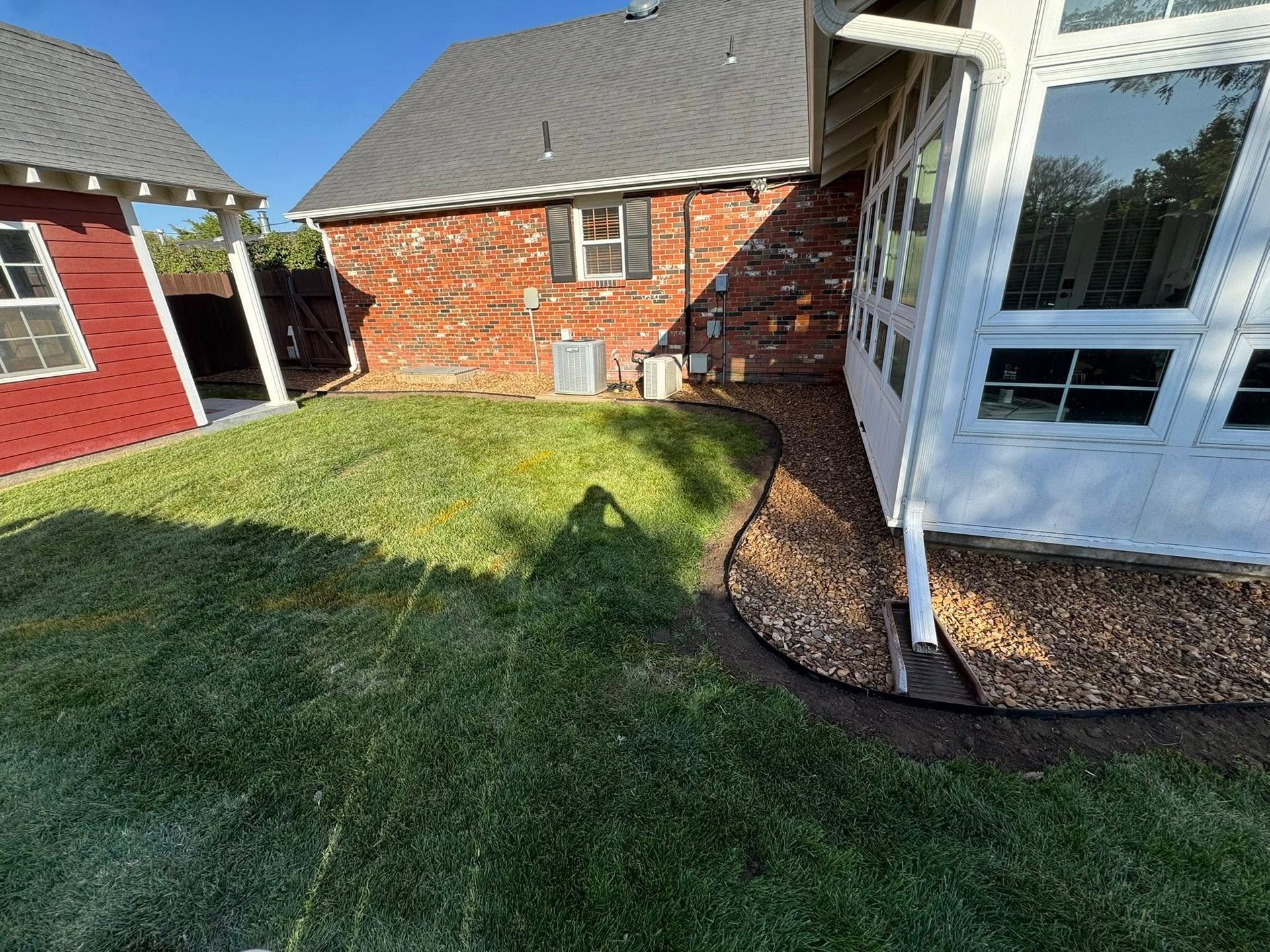 Backyard with green lawn, red brick house, and white patio doors beside a gravel border.