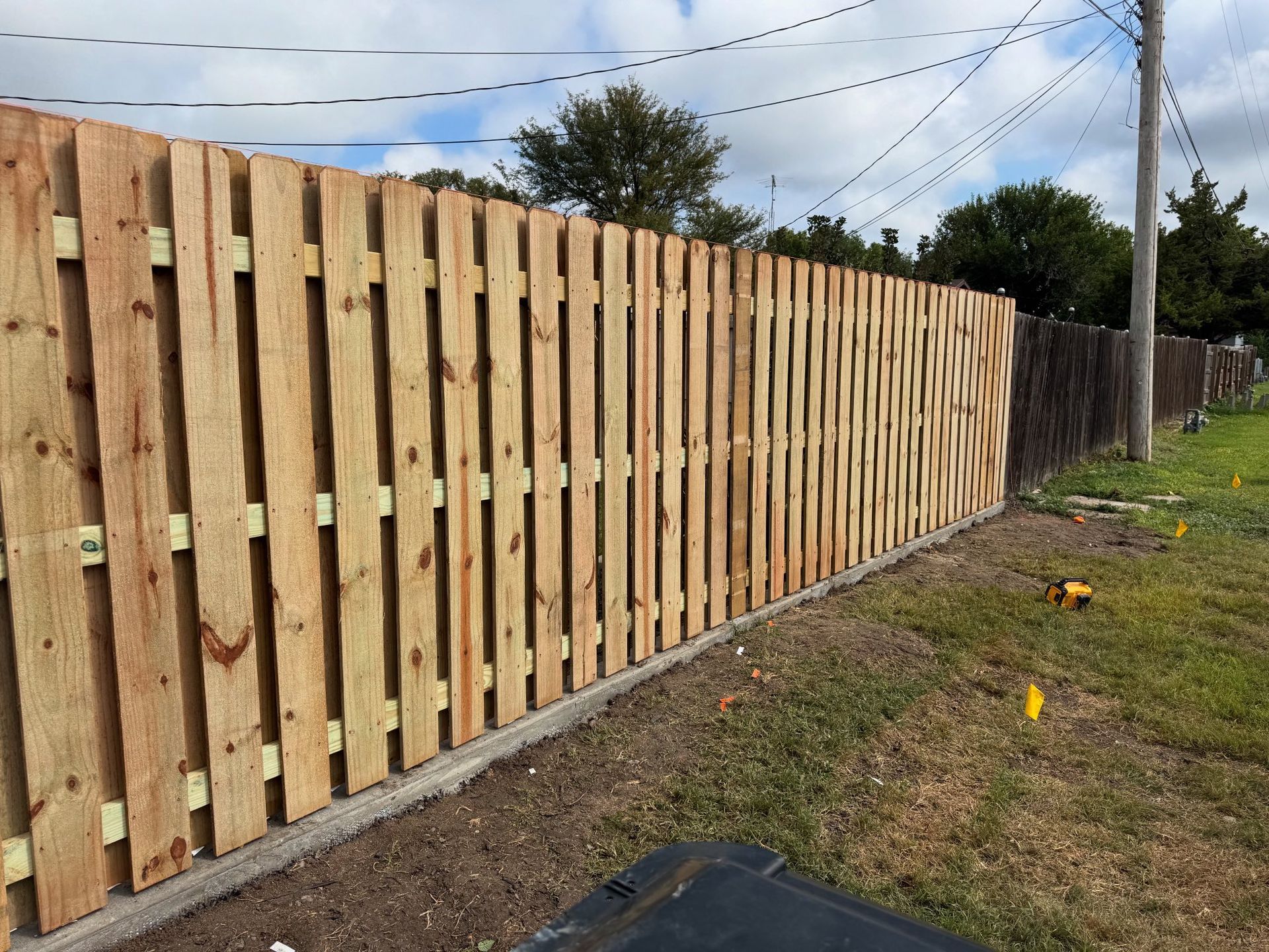 Long wooden privacy fence along a grassy yard under a partly cloudy sky