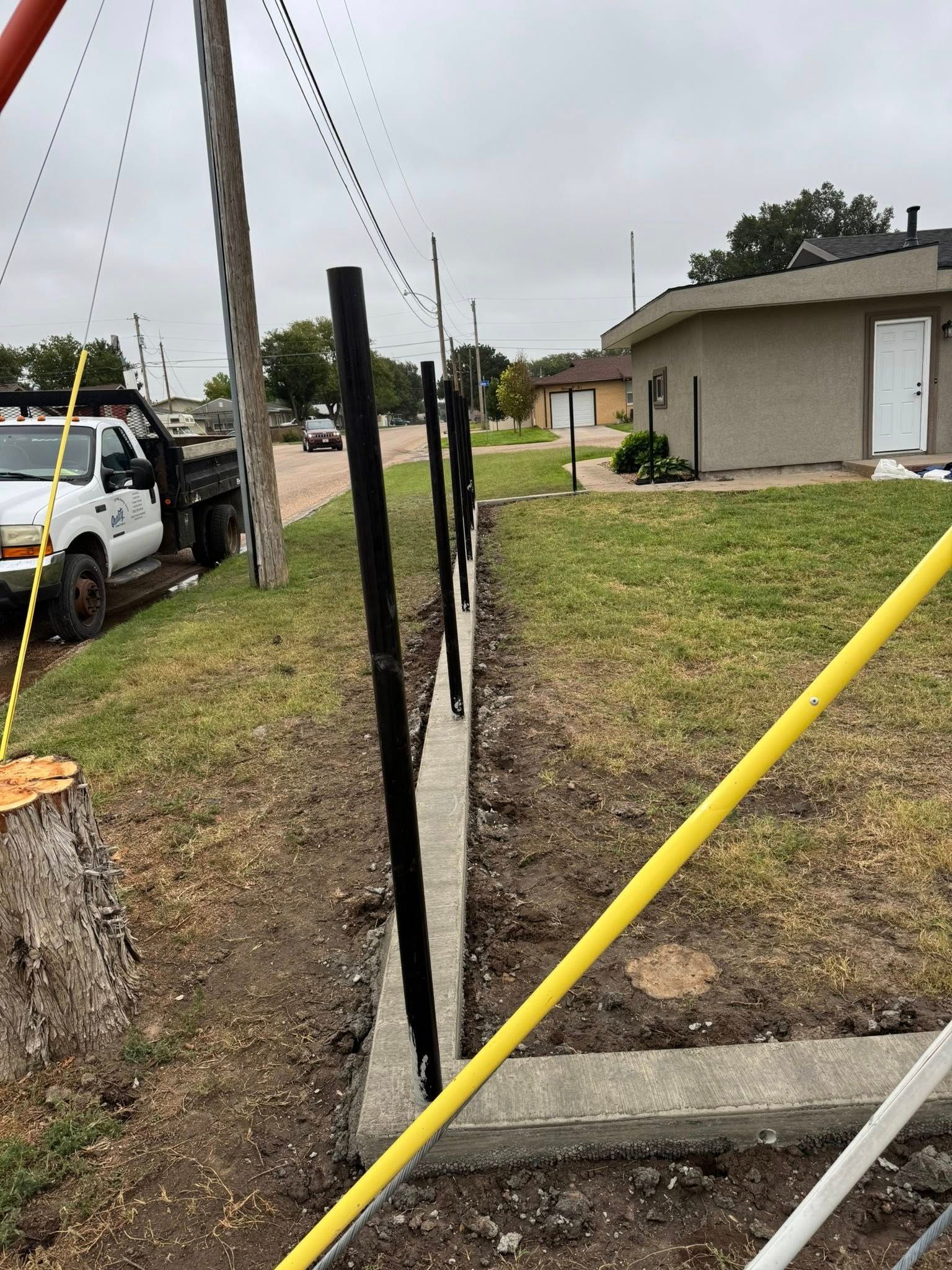 Damaged sidewalk and utility pole with exposed trench beside a house and parked truck on a cloudy day