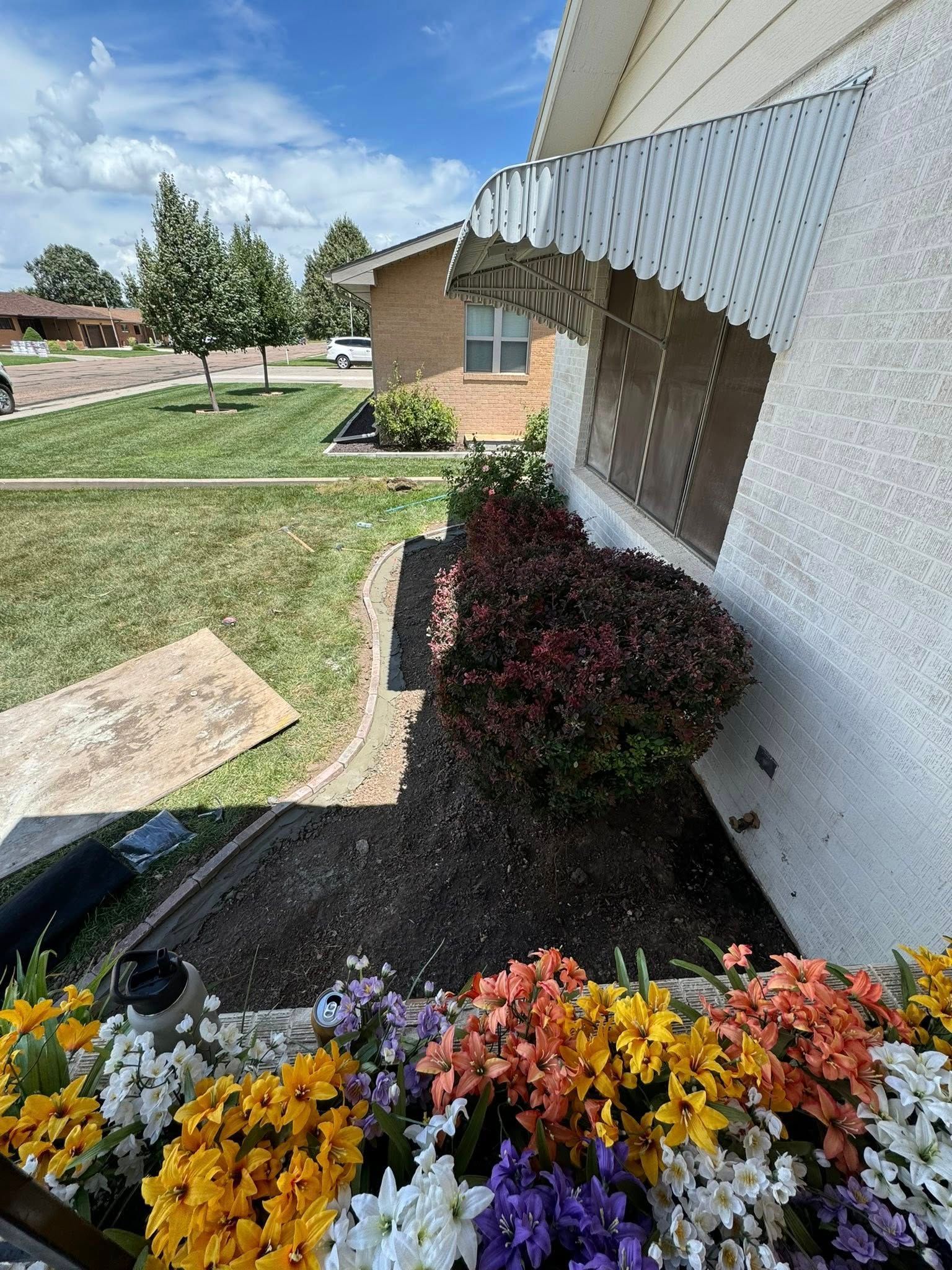 Flower bed with yellow and orange blooms beside a white house under a blue sky
