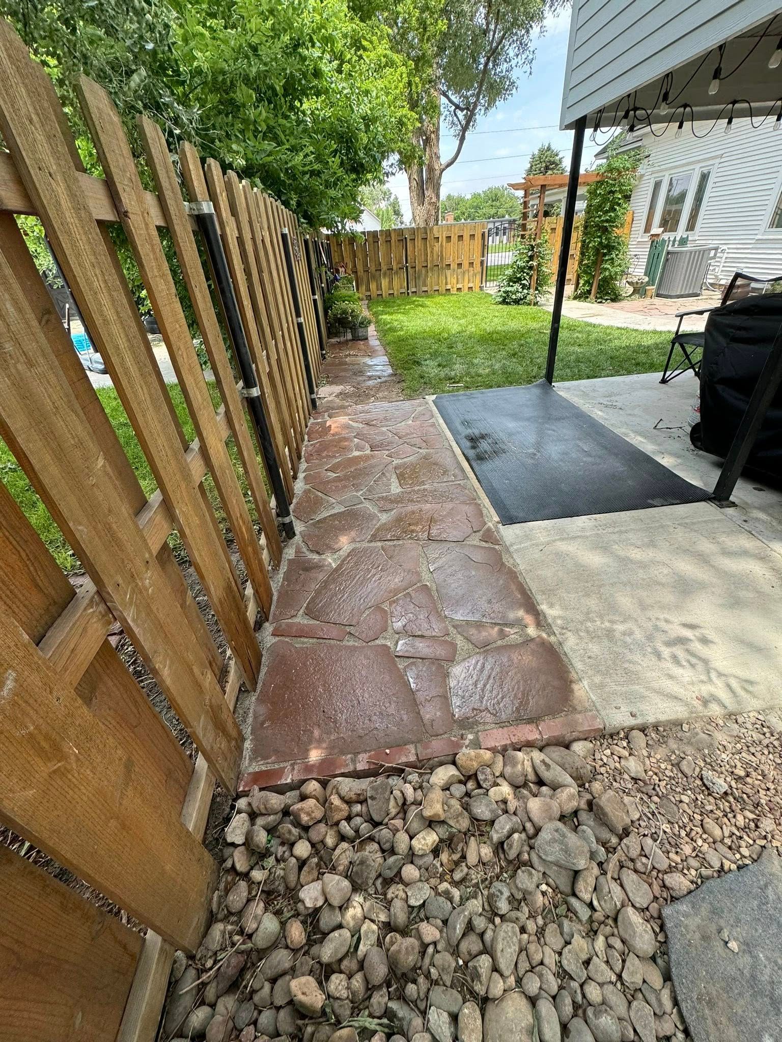 Narrow stone walkway beside a wooden fence, with gravel edging and a covered patio area.