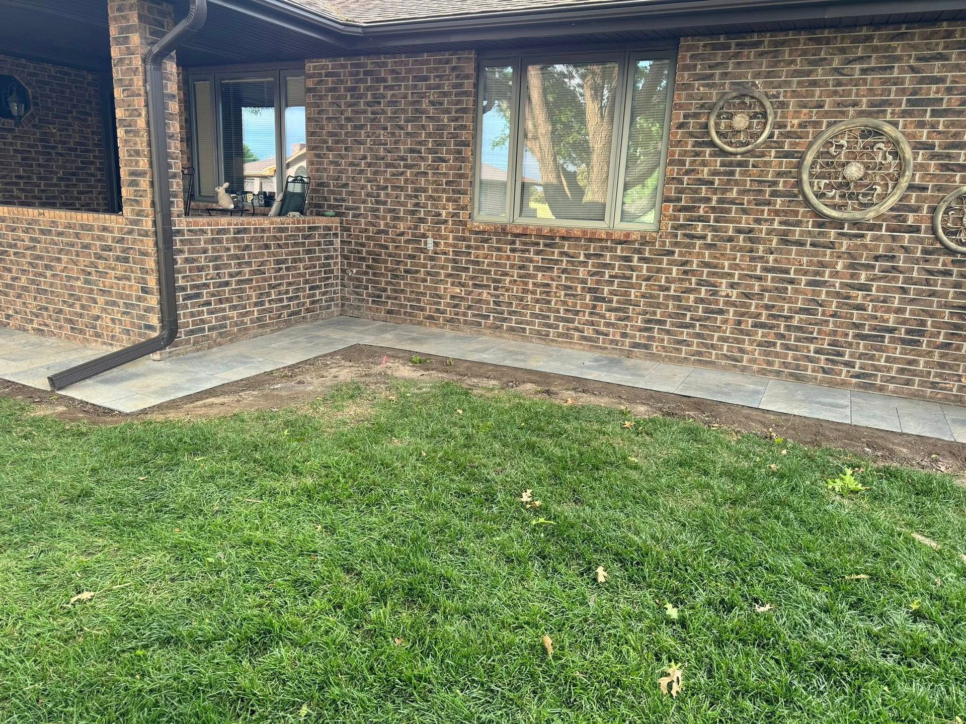 Brick house exterior with front lawn, windows, and a small concrete walkway