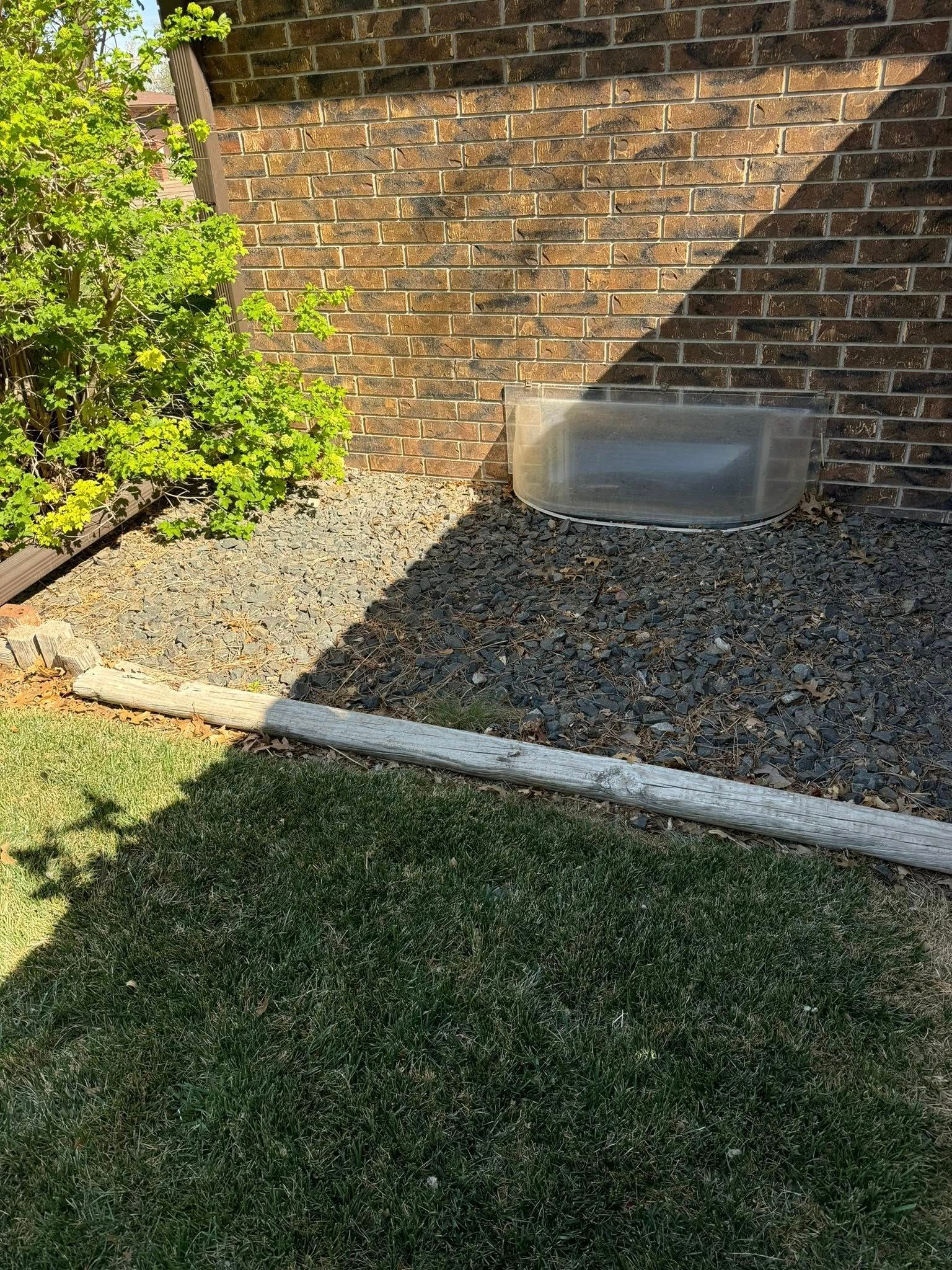Backyard with brick wall, gravel bed, shrubs, and a strip of grass in sunlight and shadow