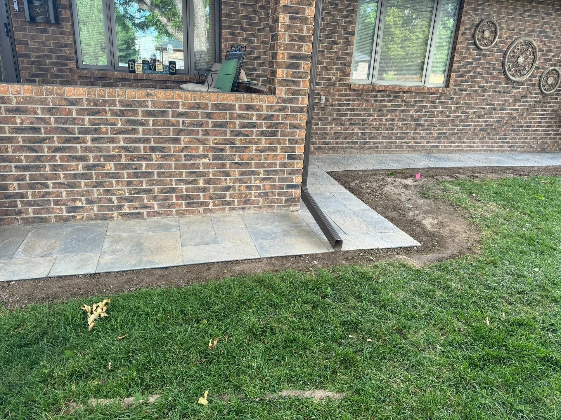Brick house exterior with a low brick wall, concrete walkway, and green lawn.