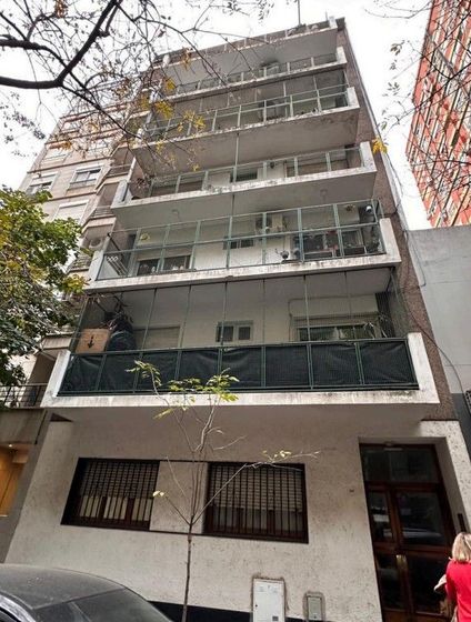 Edificio de apartamentos de mediana altura con balcones y entrada a nivel de calle, visto desde abajo.