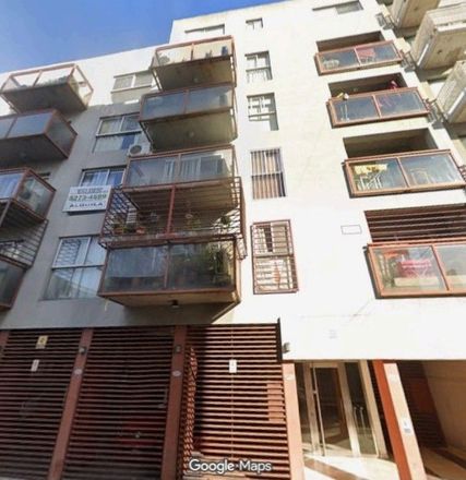 Vista de la calle de un edificio de apartamentos de color beige con balcones y contraventanas oscuras.