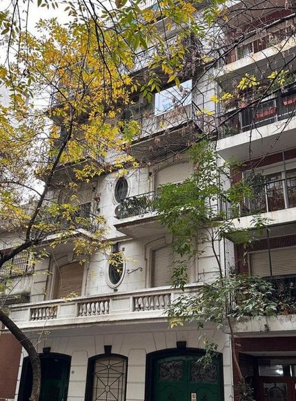 Fachada de un edificio de apartamentos con balcones y un árbol de hojas amarillas enfrente.