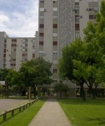 Un sendero atraviesa un patio verde bordeado de árboles, que conduce a altos edificios de apartamentos bajo un cielo nublado.