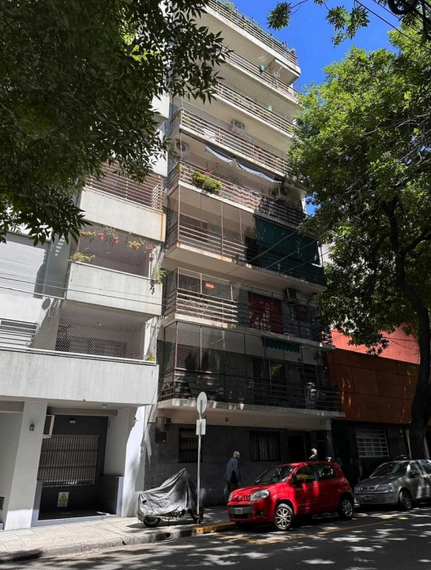 Edificio de apartamentos en una calle arbolada con coches aparcados, incluyendo un SUV rojo, a plena luz del día.