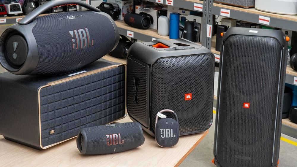 Varios altavoces portátiles JBL en color negro y gris, incluyendo modelos cilíndricos y rectangulares, colocados sobre una mesa.