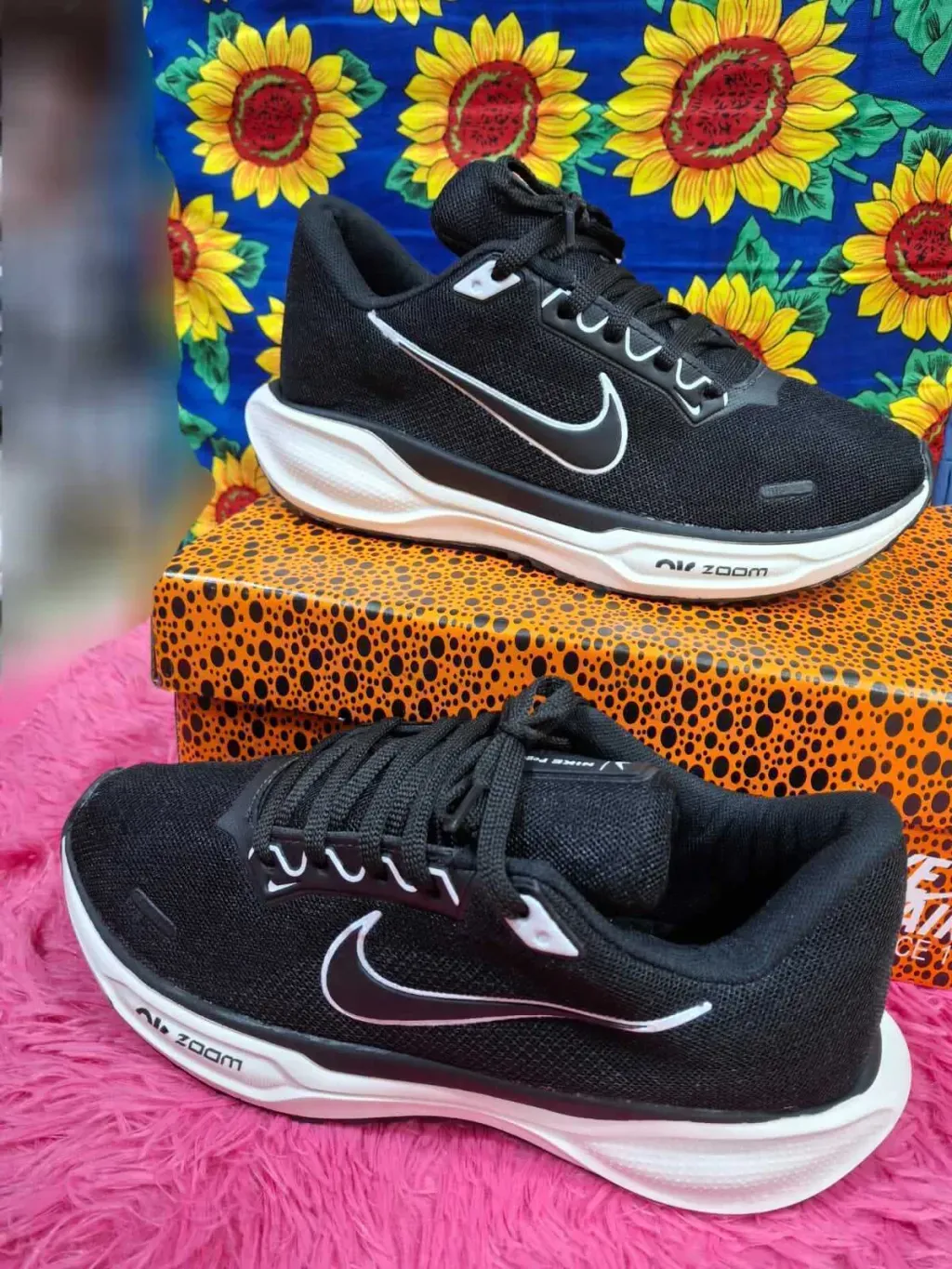 Zapatillas de running Nike negras sobre una caja con estampado de leopardo y un fondo de girasoles.