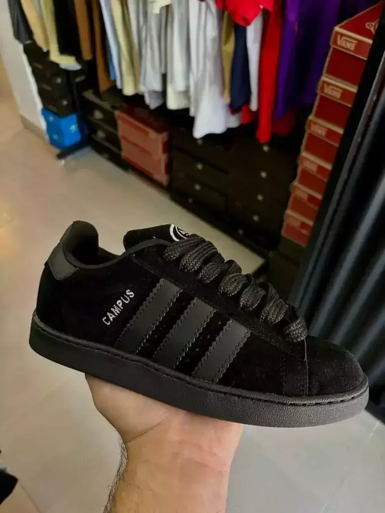 Una zapatilla Adidas negra sostenida en una mano, con ropa y cajones de un armario al fondo.