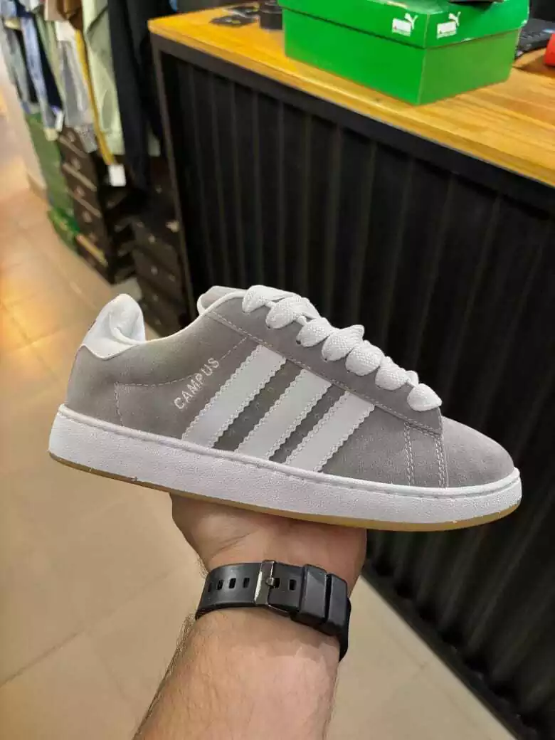Una zapatilla Adidas gris sostenida en la mano, mostrada en el interior de una tienda sobre el mostrador.