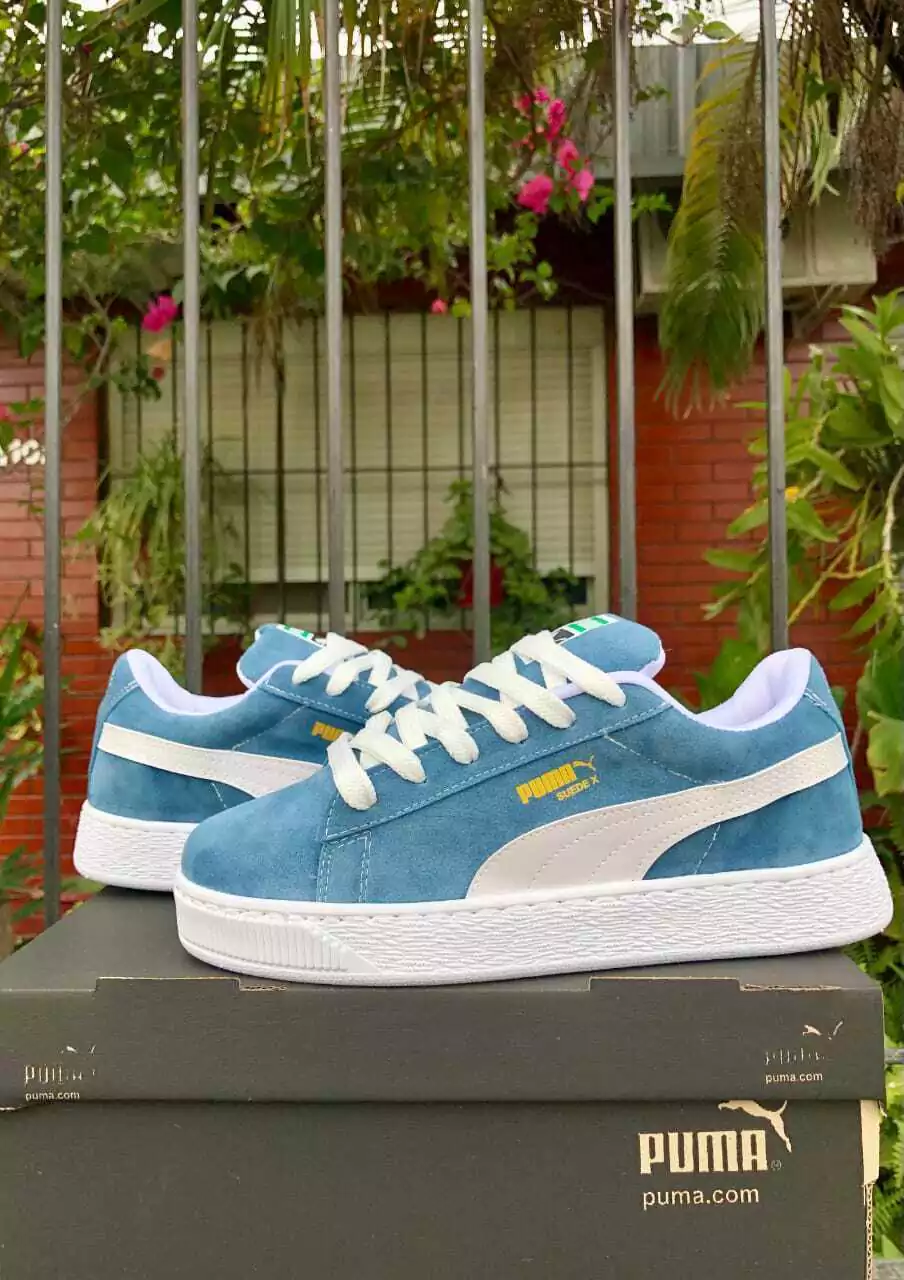 Zapatillas Puma azules con suela y cordones blancos sobre una caja de zapatos negra al aire libre.
