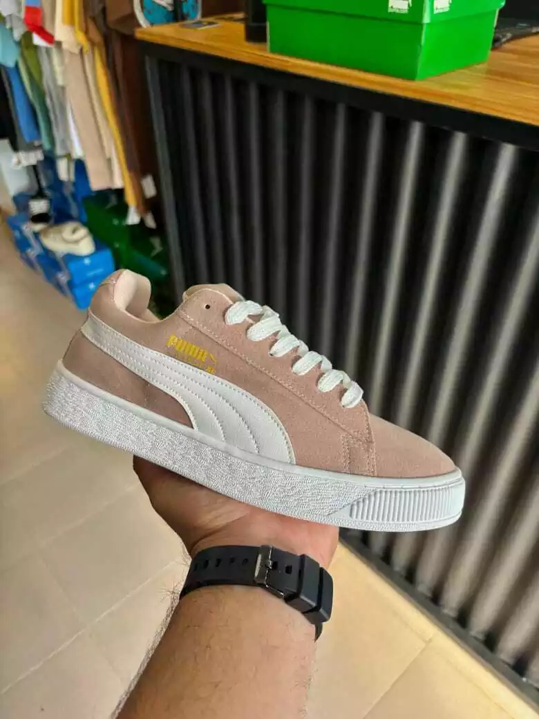 Una mano sostiene una zapatilla rosa y blanca en el pasillo de una tienda, dejando ver un reloj negro.