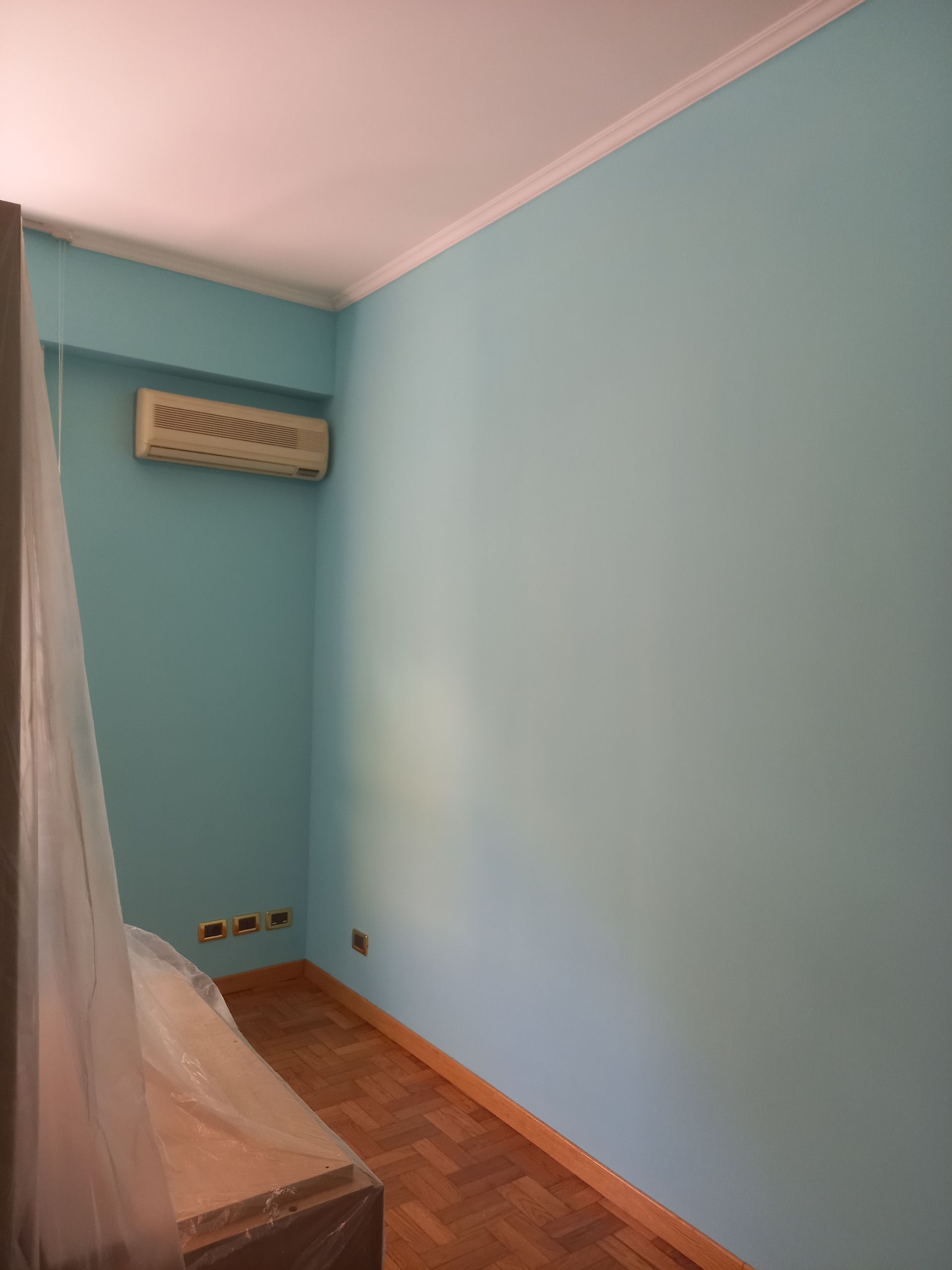 Stanza vuota di colore azzurro chiaro con pavimento in legno, finiture rosa sul soffitto e condizionatore d'aria a parete.