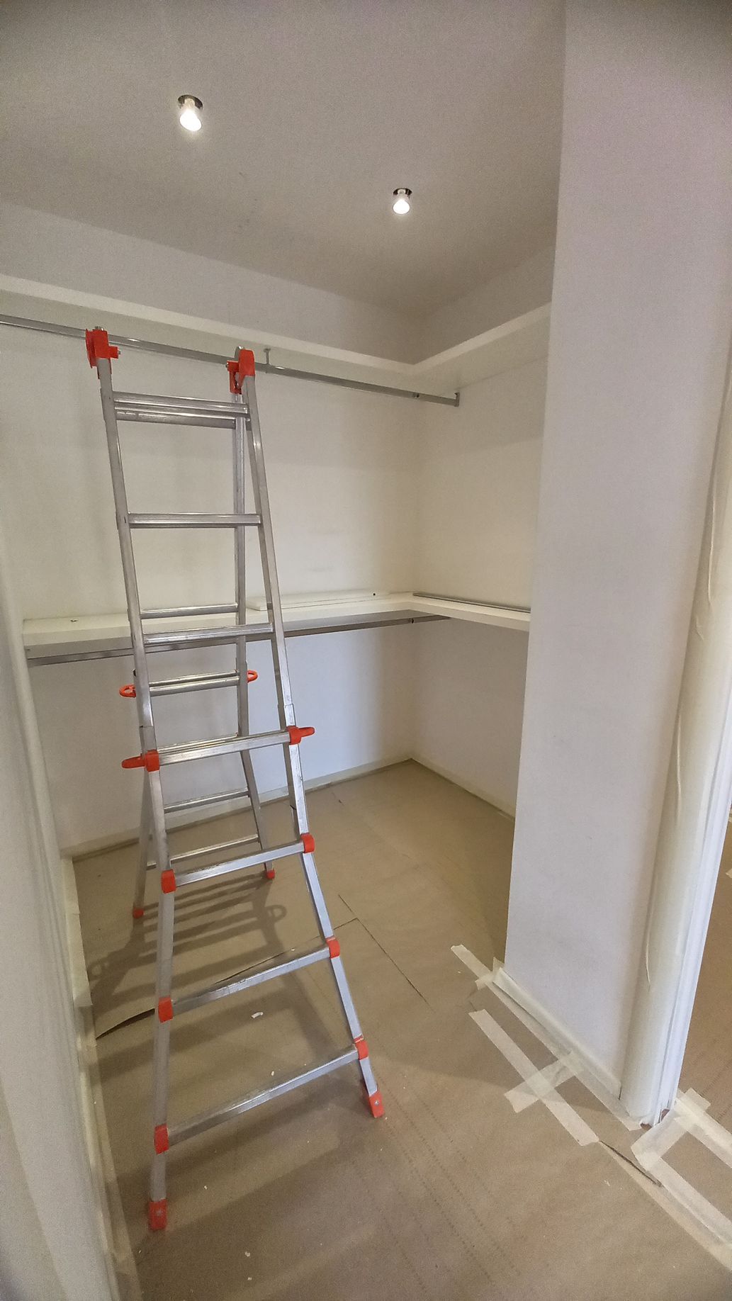 Scala alta in una stanza non rifinita con pareti bianche, pavimento beige e luci a soffitto.