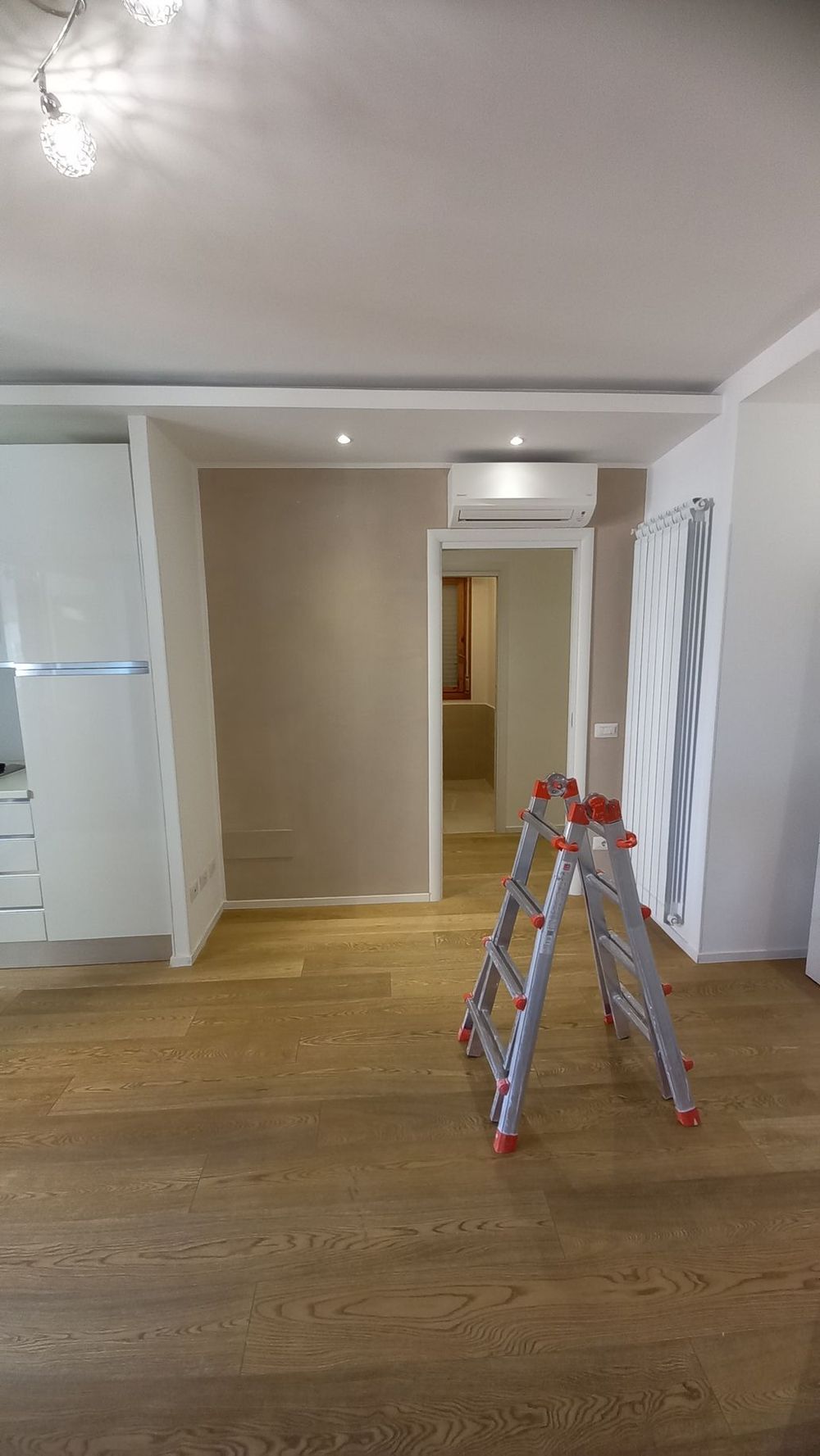 Stanza vuota con pavimento in legno, pareti beige e una scala a pioli rossa vicino al centro.