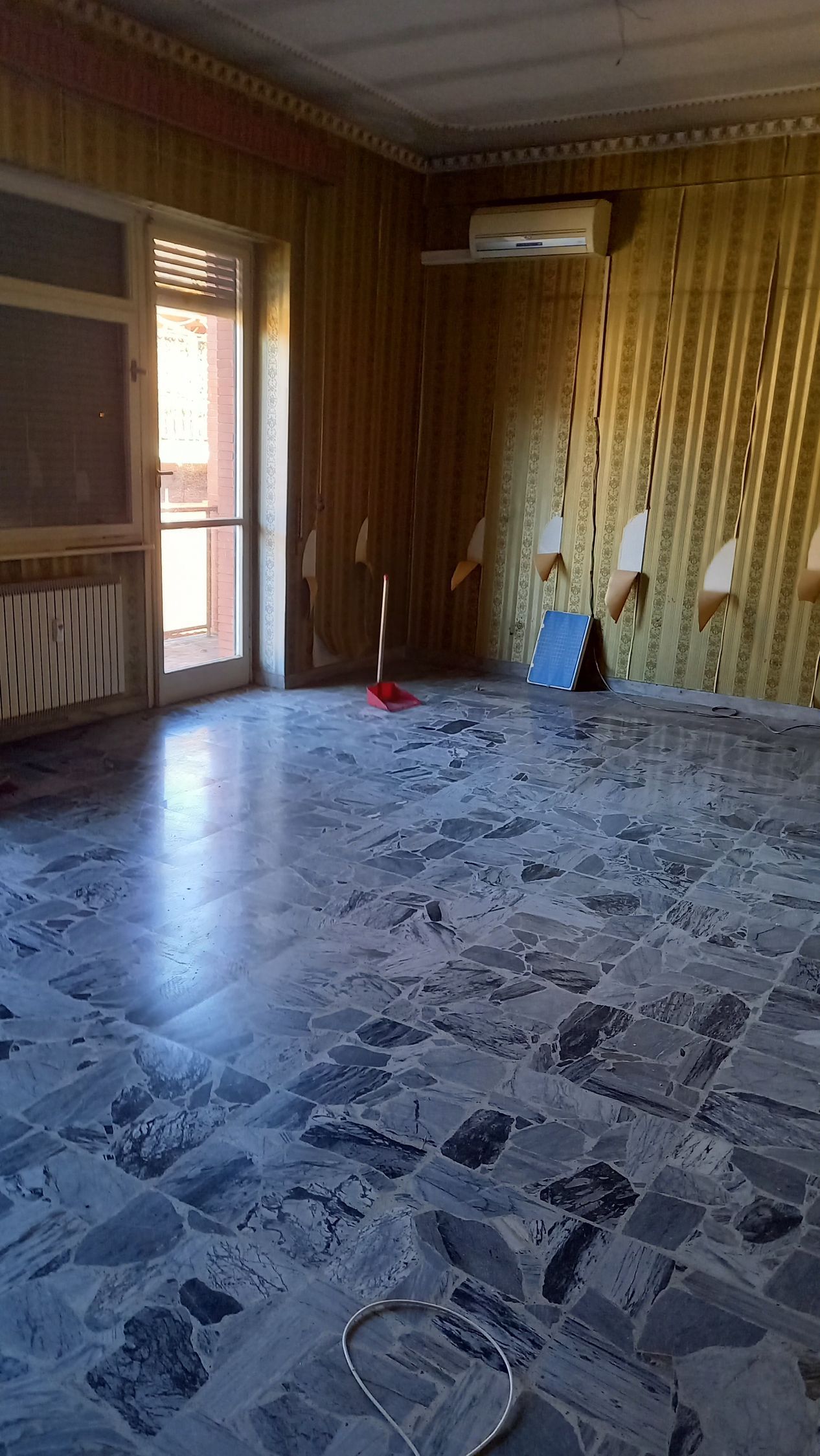 Stanza vuota con pavimento piastrellato decorato, pareti rivestite in legno e una porta aperta che lascia entrare la luce naturale.