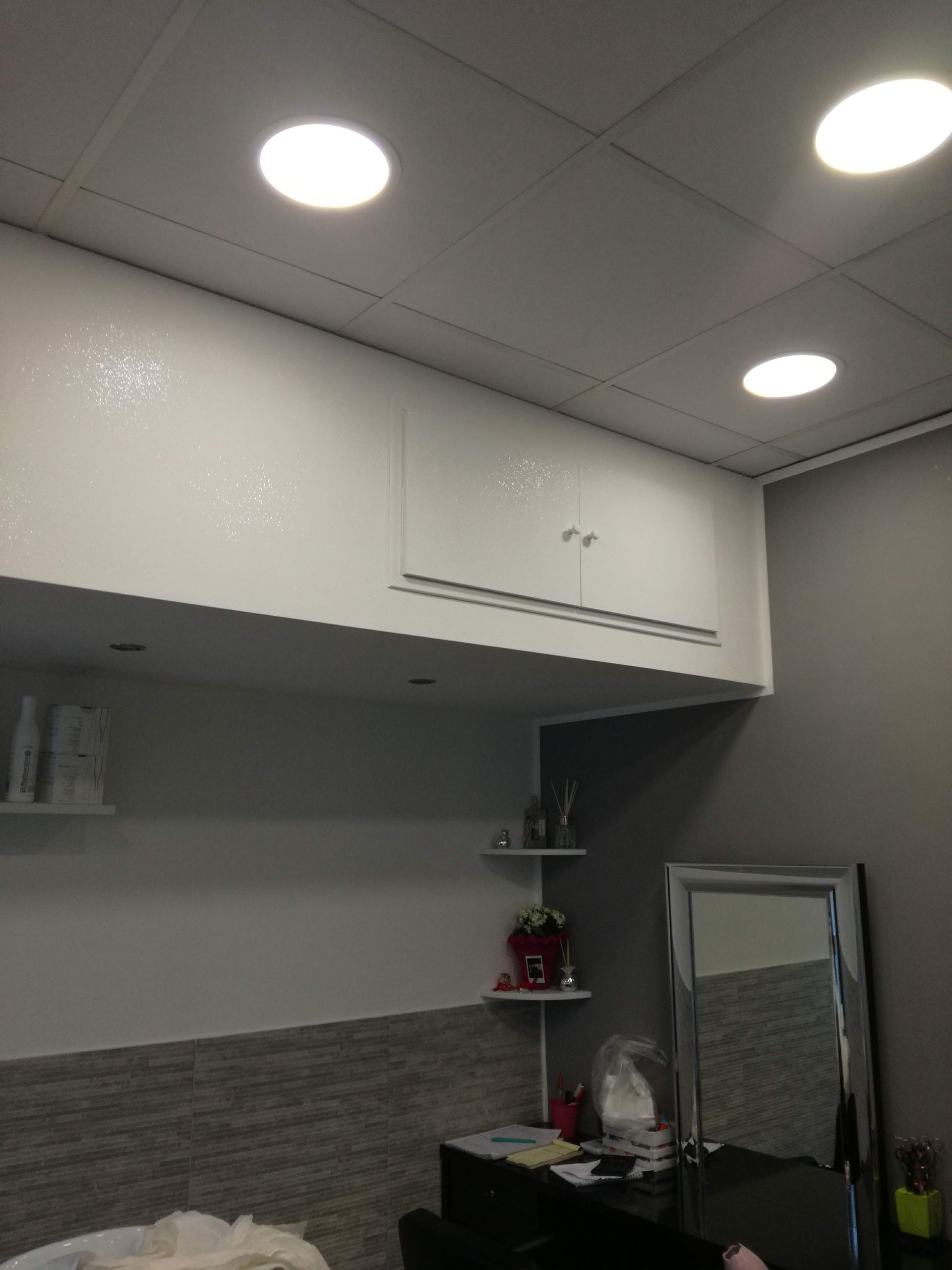Piccolo angolo cottura adibito a ufficio, con mobili bianchi, pareti grigie, lampade rotonde a soffitto e uno specchio appoggiato.