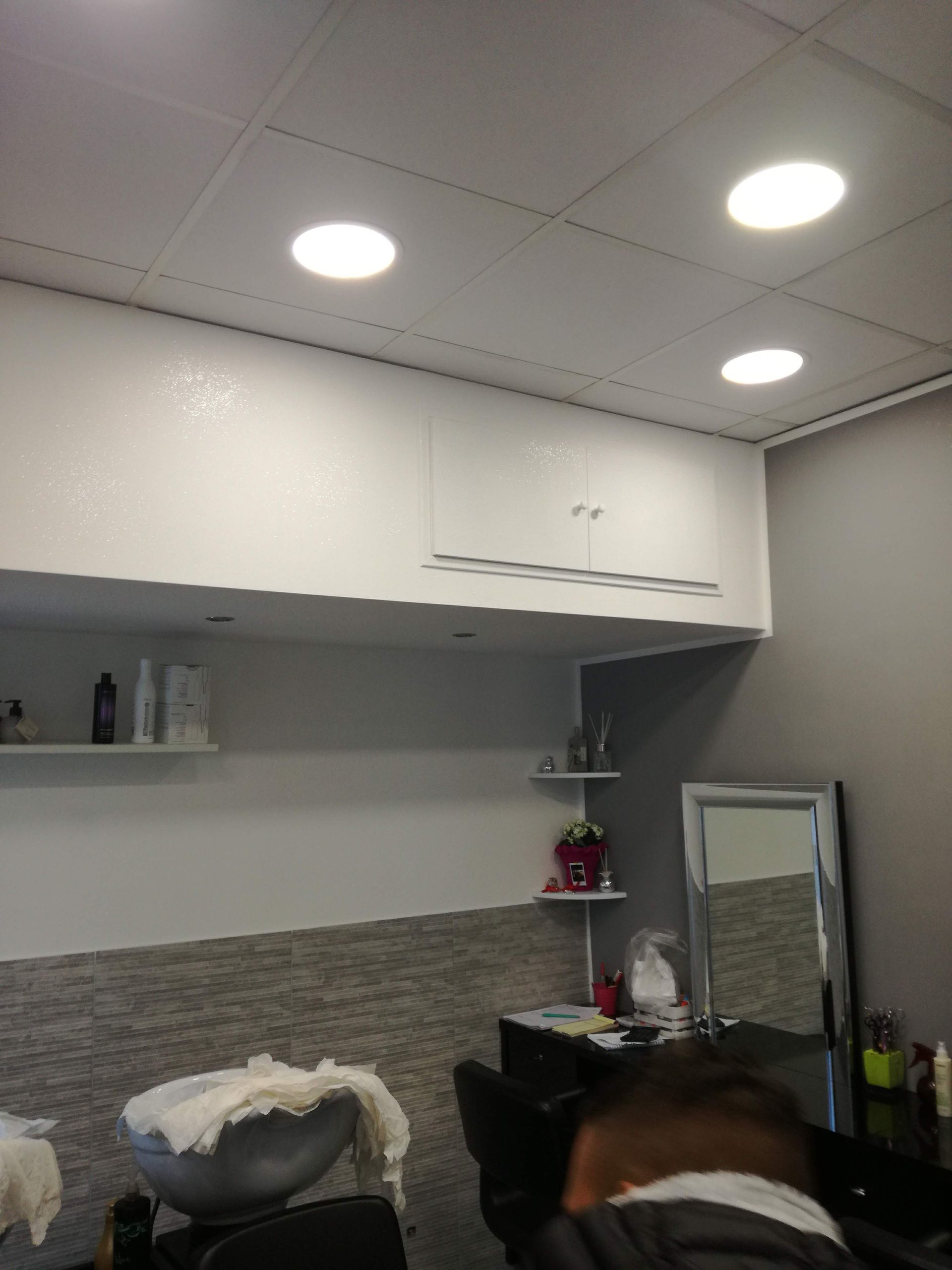 Zona lavabo del salone con mobili bianchi, parete piastrellata in grigio, specchio e faretti a incasso a soffitto.