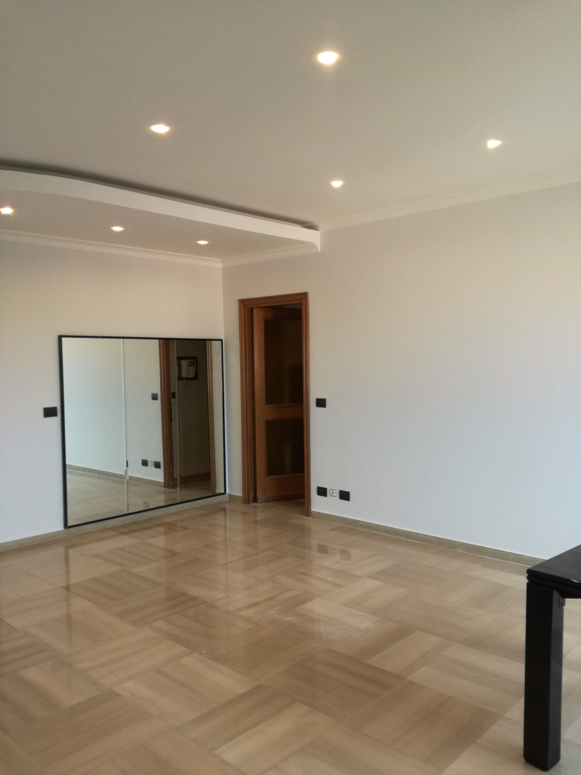 Stanza moderna vuota con pavimento in legno chiaro, faretti a incasso a soffitto, armadio con ante a specchio e porta aperta.