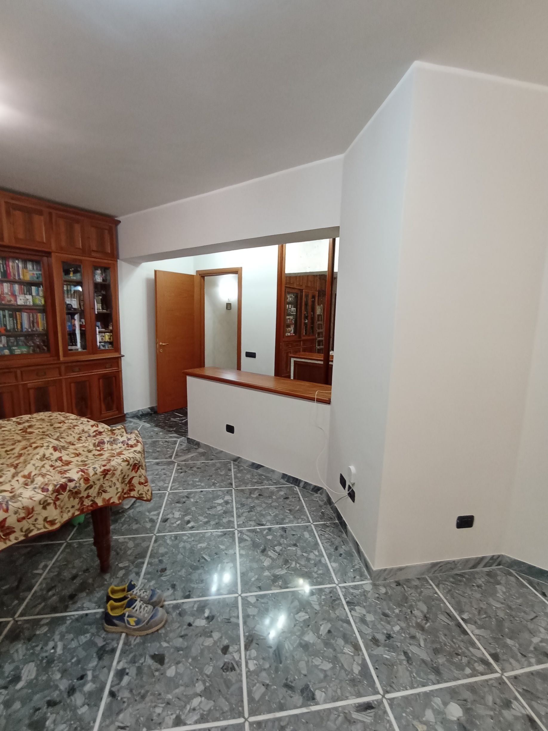 Soggiorno con pavimento piastrellato grigio, mobili in legno, uno specchio e una porta aperta su un corridoio